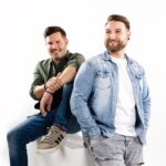 Das österreichische Musikduo Edmund vor weißem Hintergrund – einer sitzt entspannt, der andere steht lächelnd daneben.